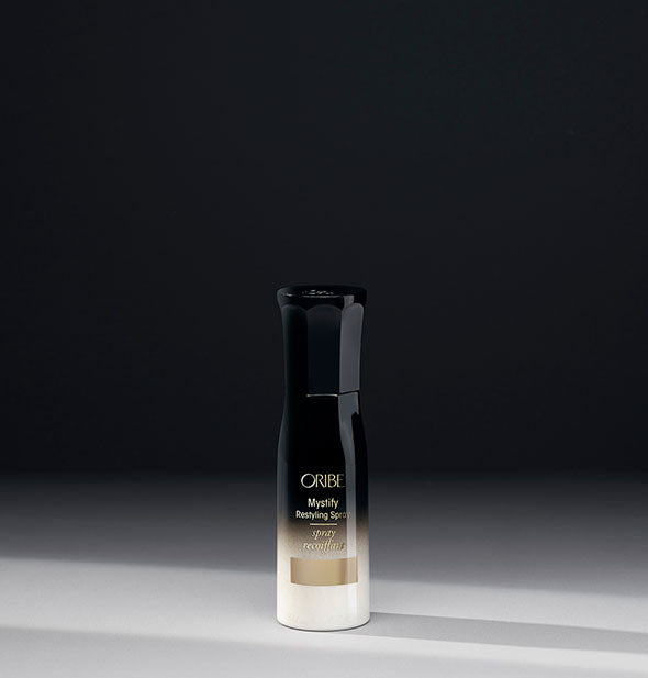 Small white-to-black bottle of Oribe Mystify Restyling Spray on gray background
