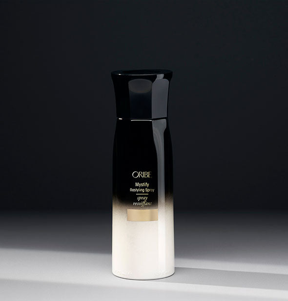 White-to-black bottle of Oribe Mystify Restyling Spray on gray background