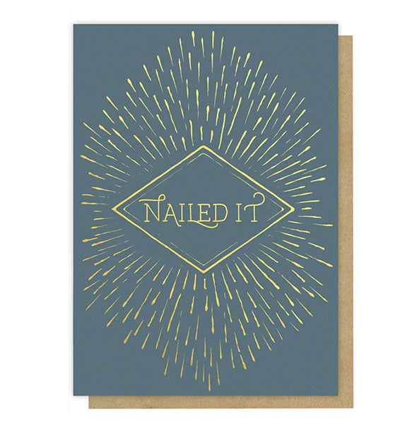 Muted teal greeting card says, "Nailed It" in metallic gold lettering inside a diamond border surrounded by radiating gold lines
