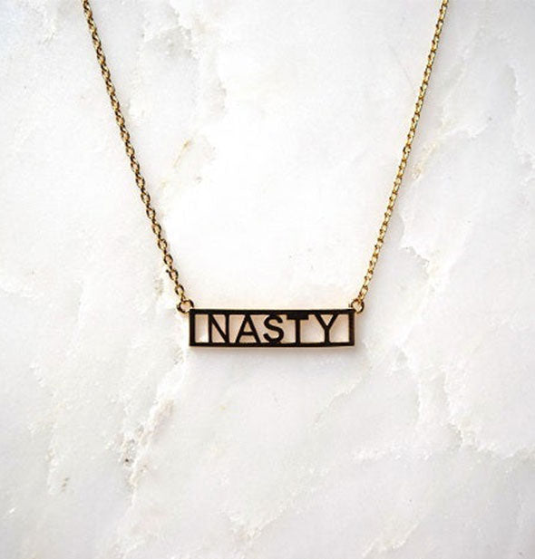 Gold bar necklace on white marble surface says, "Nasty"