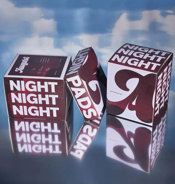 Boxes of August brand Night Pads on a reflective backdrop of blue sky with clouds