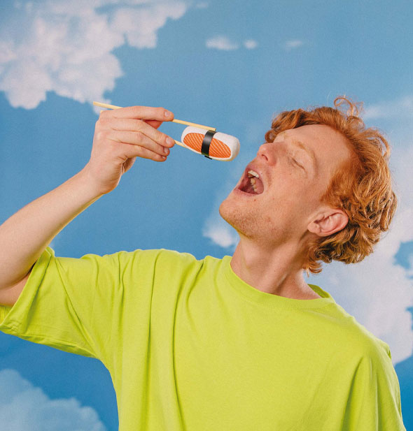 Model holds a rolled-up sushi socks between chopsticks over his open mouth in front of a blue sky with clouds backdrop