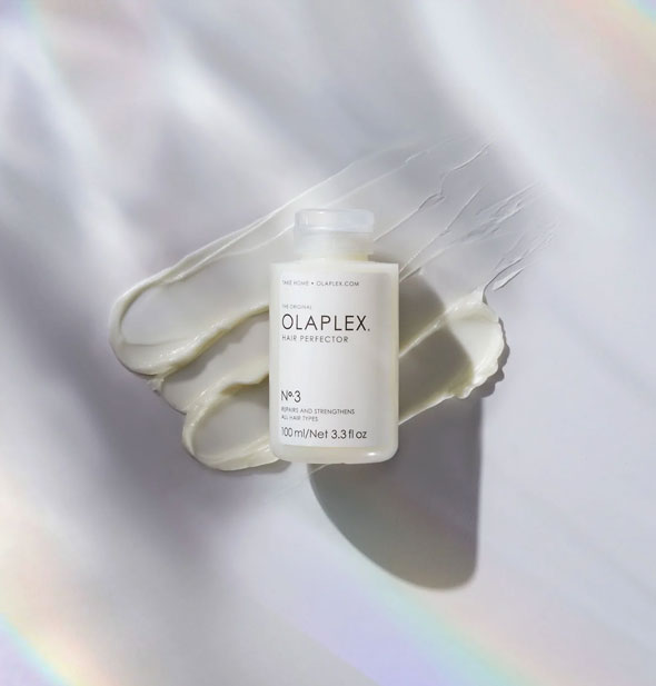 Bottle of Olaplex No. 3 Hair Perfector rests on product sample swabs on an iridescent surface