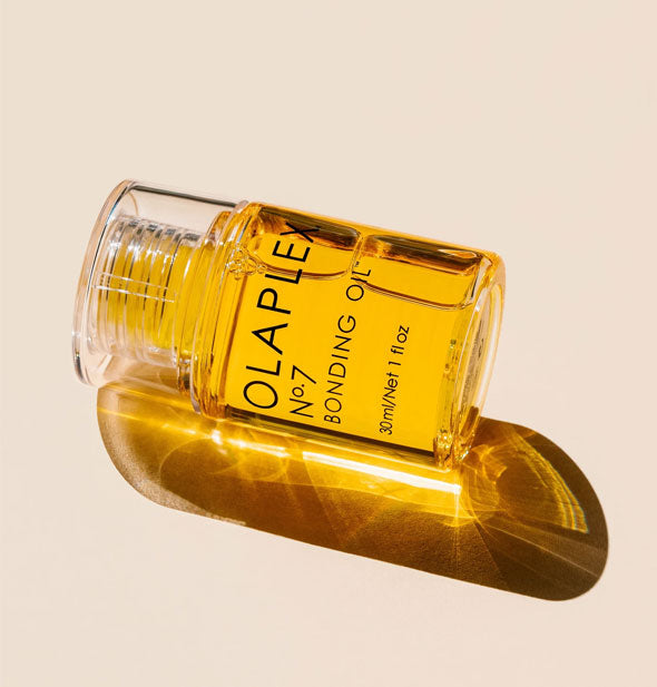 Sunlight shines through a bottle of golden Olaplex No. 7 Bonding Oil