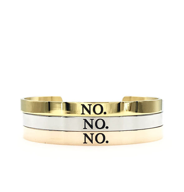 Three metal bangles in gold, silver, and rose gold finishes stacked on top of one another are each printed with, "No."