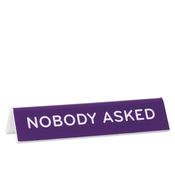 Rectangular purple desk placard says, "Nobody asked" in white lettering