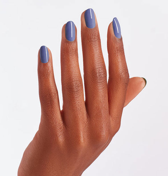 Model's hand wears a shade of dark periwinkle blue nail polish