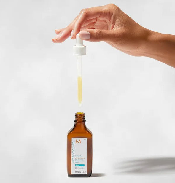 Model's hand lifts the dropper from a bottle of Moroccanoil Oily Scalp Treatment