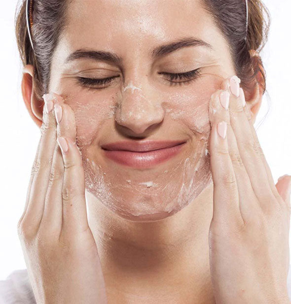 Squinting model applies face scrub to cheeks