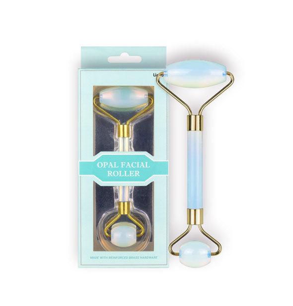 Double-ended blueish opal stone facial roller with gold hardware next to its packaging
