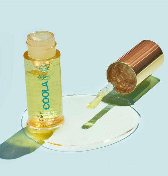An opened tube of Coola Liplux Hydrating Oil with some product spilled out to show color and texture