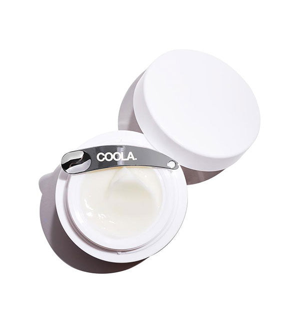 Pot of Coola moisturizer with metallic applicator spatula