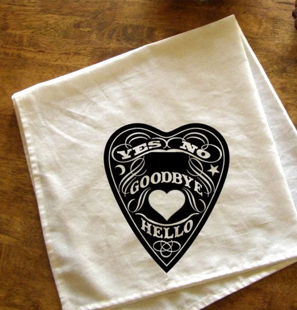 White towel with black Ouija board inspired design lays folded on a wooden tabletop