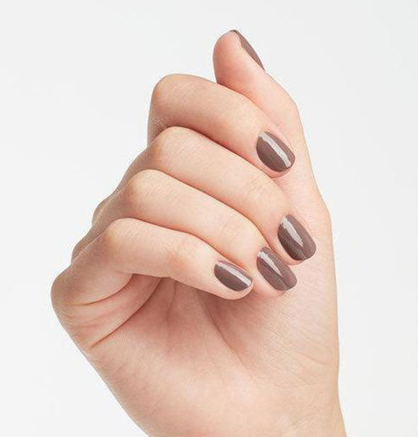 Model's hand wears a taupe shade of nail polish