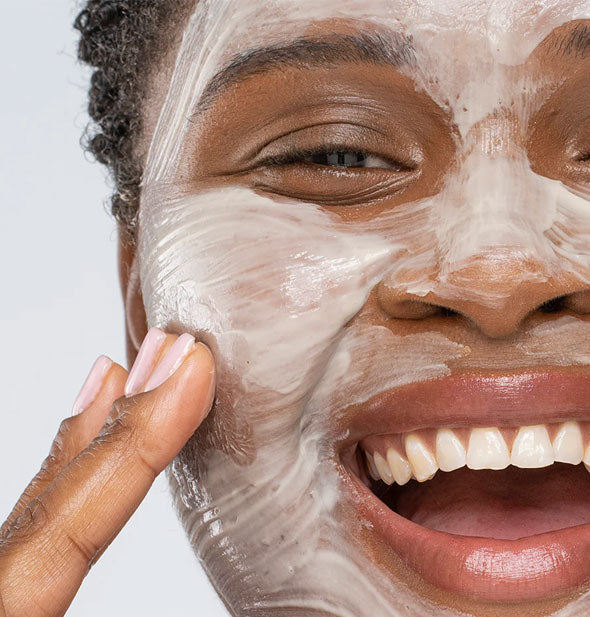 Smiling model applies mask to cheek with fingertips