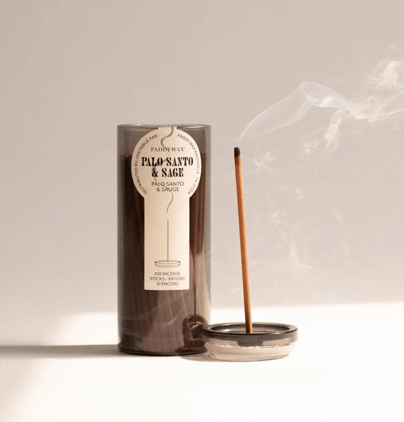 Lid removed from a glass tube of Paddywax Palo Santo & Sage incense sticks doubles as a holder for one burning stick