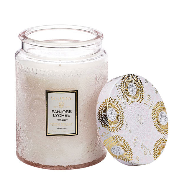 Whitish embossed glass Panjore Lychee Voluspa jar candle with metallic white and gold lid removed and set to the side