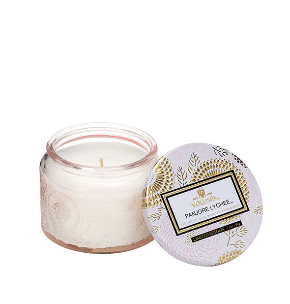 White embossed glass Panjore Lychee Voluspa candle jar with metallic floral lid set to the side
