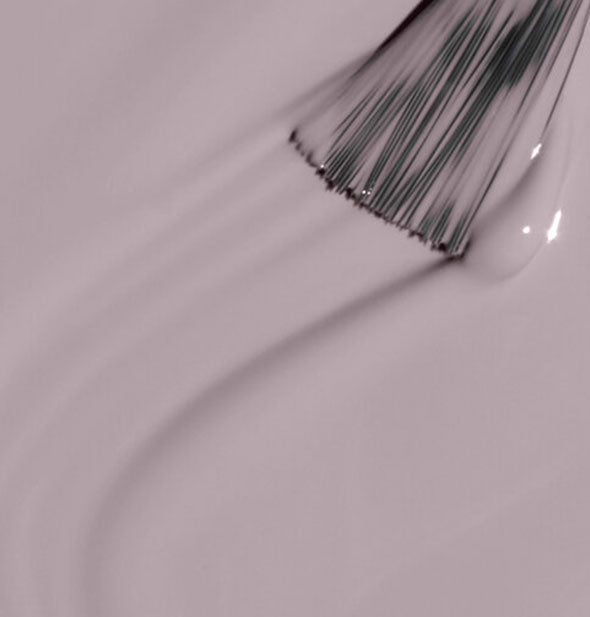 A brush tip glides through an application of purplish-grey nail polish