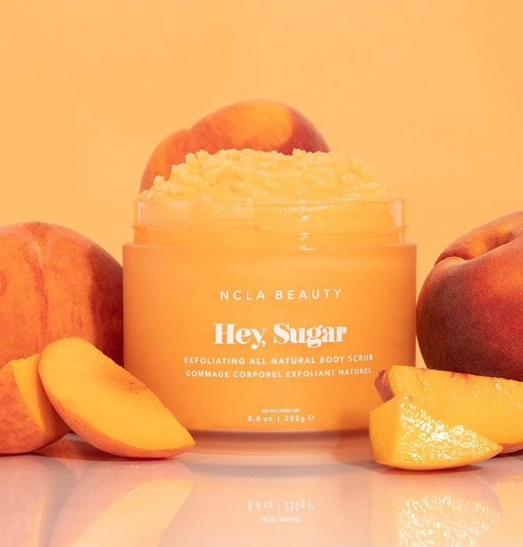 Jar of NCLA Beauty Hey, Sugar body scrub staged with whole and sliced peaches