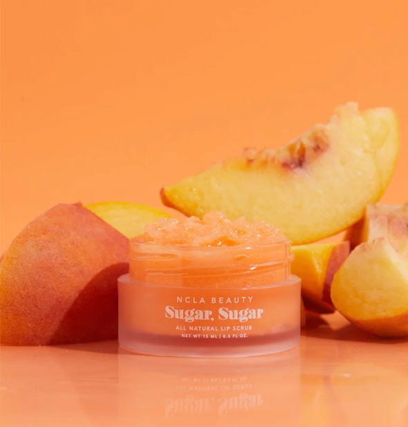 Pot of orange NCLA Beauty Sugar, Sugar All Natural Lip Scrub is flanked by pieces of a peach