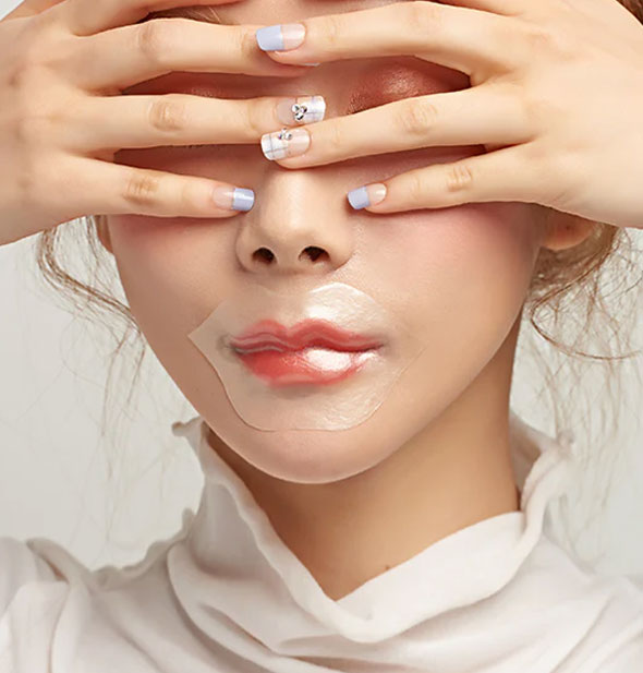 Model covering eyes wears a pearlescent patch over lips
