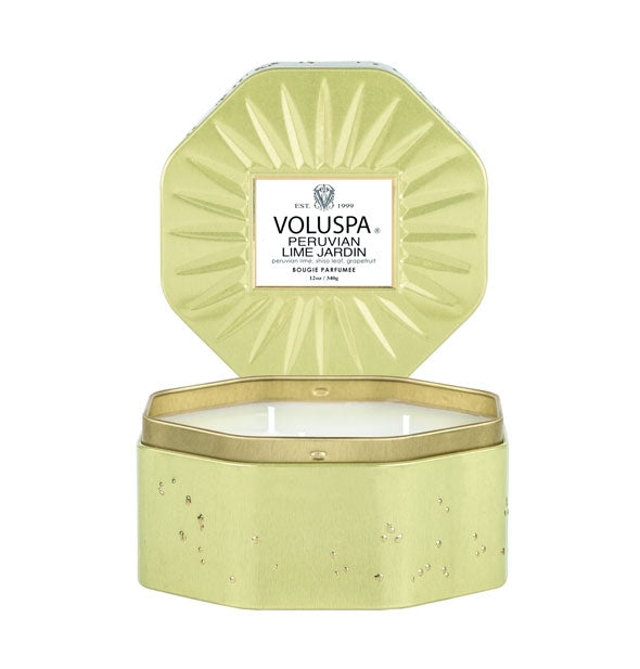 Octagonal green Voluspa Peruvian Lime Jardin tin candle with gold rim and a speckled texture with its embossed lid propped behind