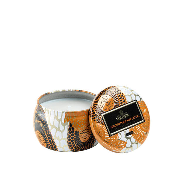 Unlit candle in a small, rounded tin with black, white, orange, and metallic design accents.