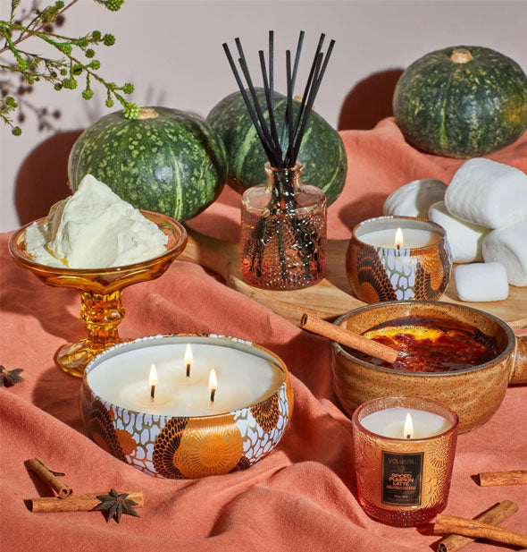 Decorative tin candles and embossed glass jar candle with various spices and botanicals on coral linen