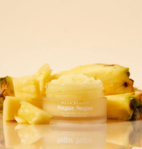 Pot of yellow NCLA Beauty Sugar, Sugar All Natural Lip Scrub is flanked by pieces of pineapple