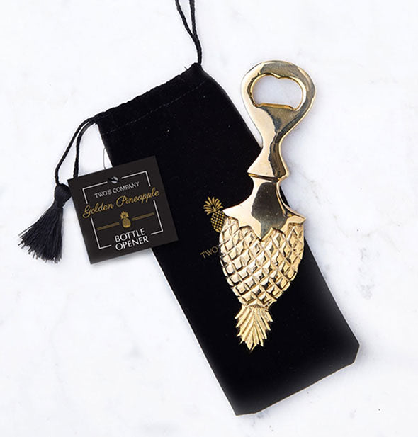 Gold-toned pineapple-shaped bottle opener atop a black drawstring pouch