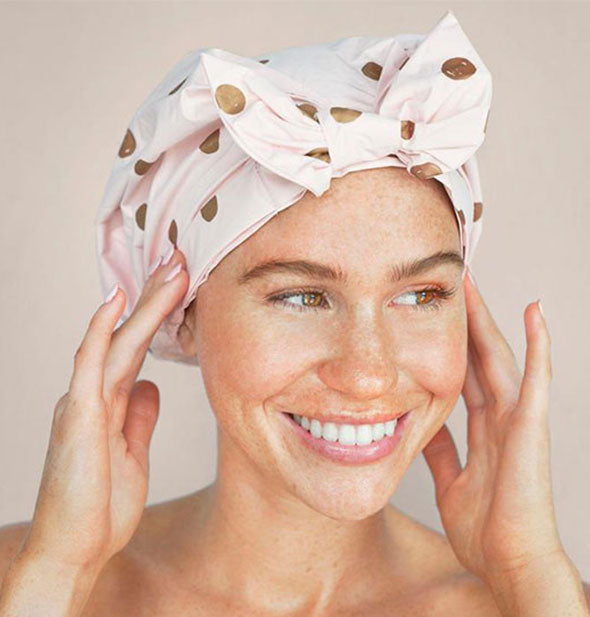 Model wears a light pink and gold dot printed shower cap with bow
