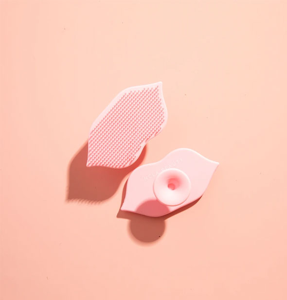 Pink lip-shaped scrubber shown from front textured side and back side with knob handle