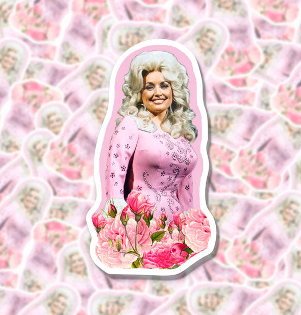 Sticker with image of Dolly Parton wearing a pink dress with pink flowers at the bottom rests on a blurred backdrop of others like it