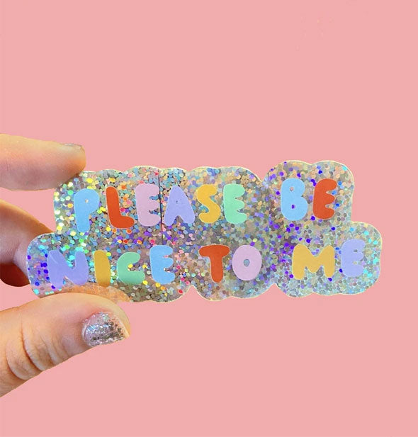 Model's hand holds a Please Be Nice to Me sticker with colorful bubble lettering on a holographic glitter background