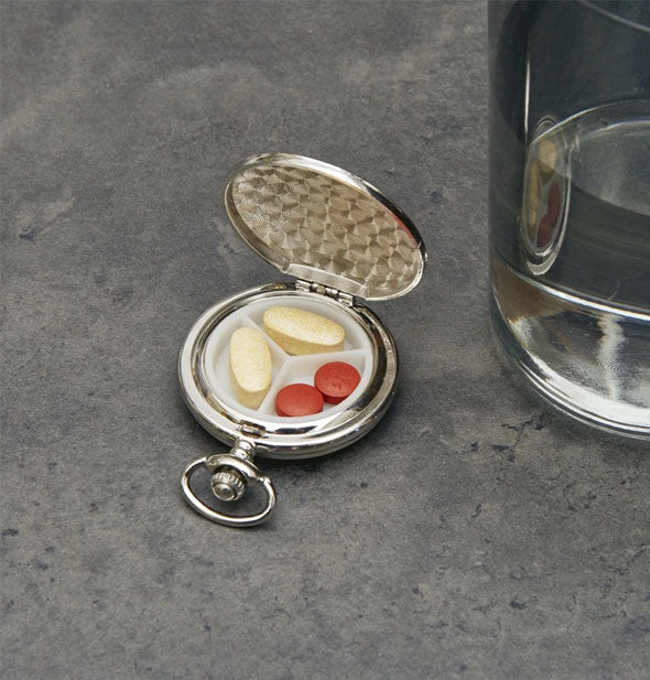 Round silver-toned pill case that resembles a pocket watch features three interior compartments