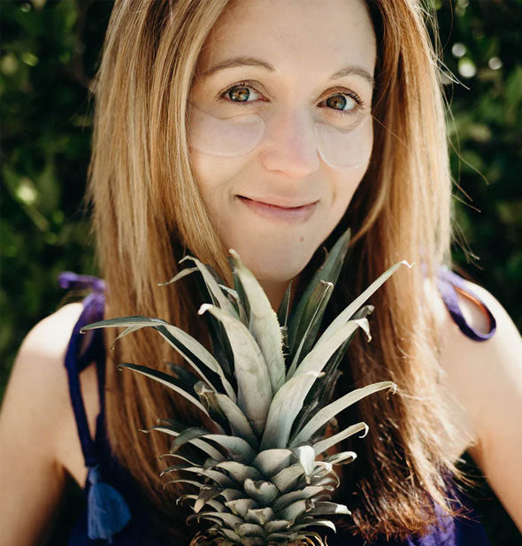 Smiling model holding a pineapple wears a pair of under-eye patches