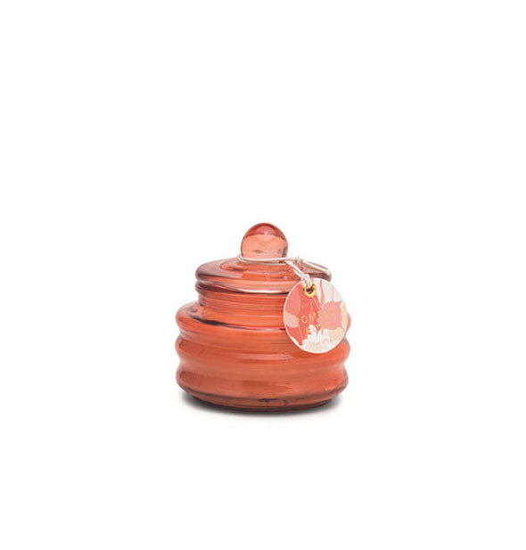 Small rose-colored ribbed glass candle jar with knobbed lid and tag attached