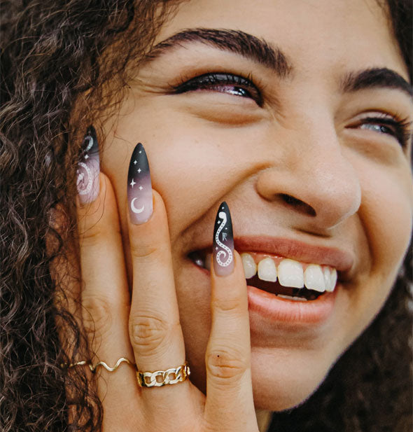 Smiling model with hand to face wears extra-long stiletto Potion style Rave Nailz
