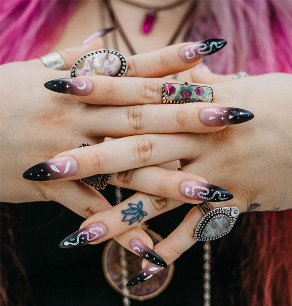 Model's crossed fingers feature extra-long black and white ombre nails with snake and celestial designs