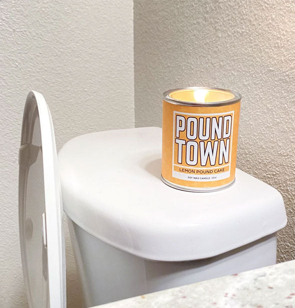 Yellow Pound Town paint can candle sits on top of a toilet tank