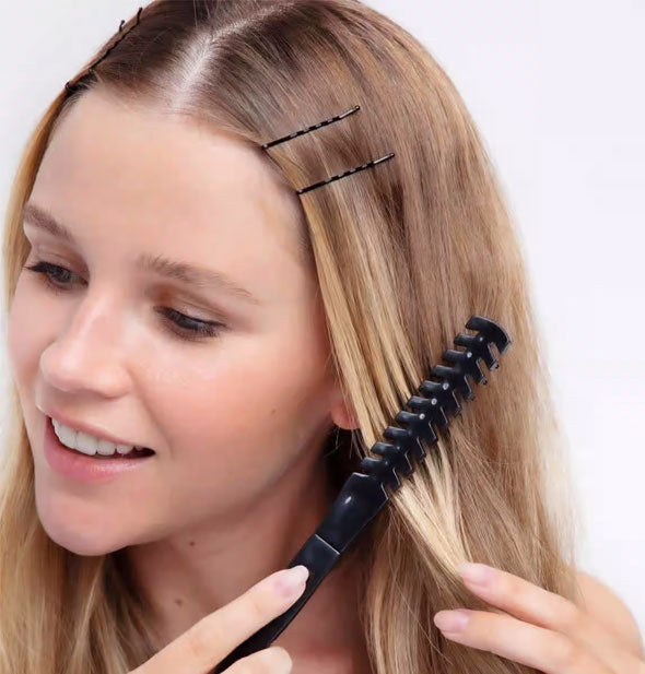 Model with bobby pins holding a front section of hair back runs a brush.comb through bottom lengths