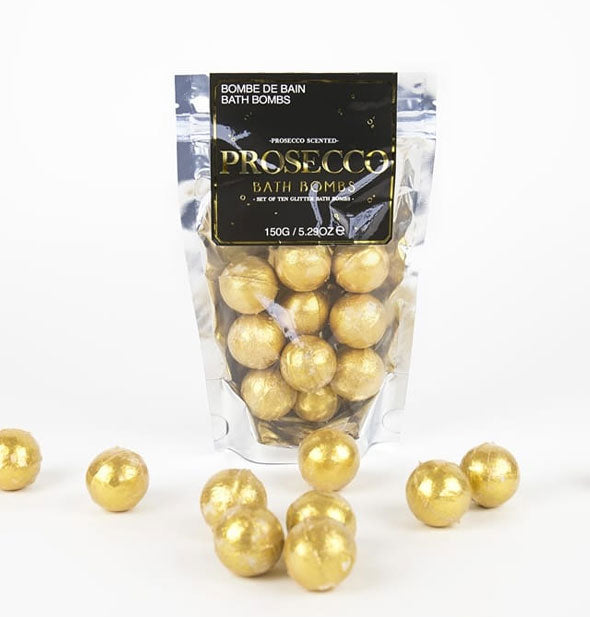 Silver and black bag of Prosecco Bath Bombs with clear window through which golden orbs can be seen; several bath bombs lay in front and to the sides