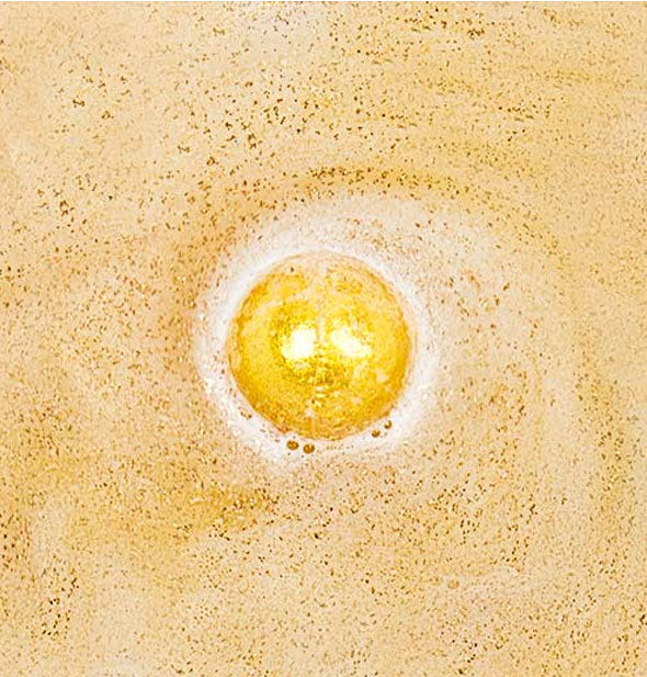 Gently fizzing round gold bath bomb in bubbly water