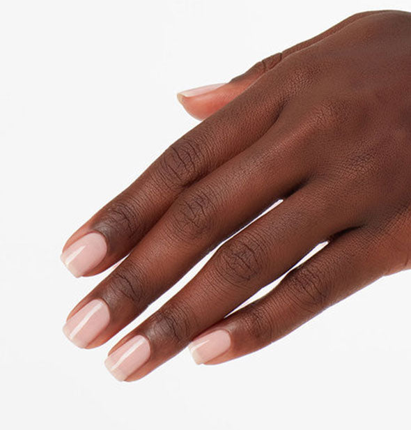 Model's hand wears a sheer pink shade of nail polish