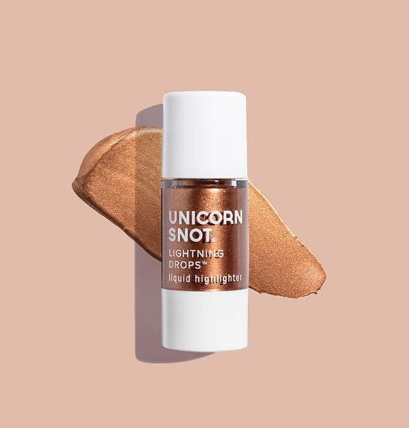 Bottle of Unicorn Snot Lightning Drops Liquid Highlighter in the shade Queen with sample application on a light peach surface