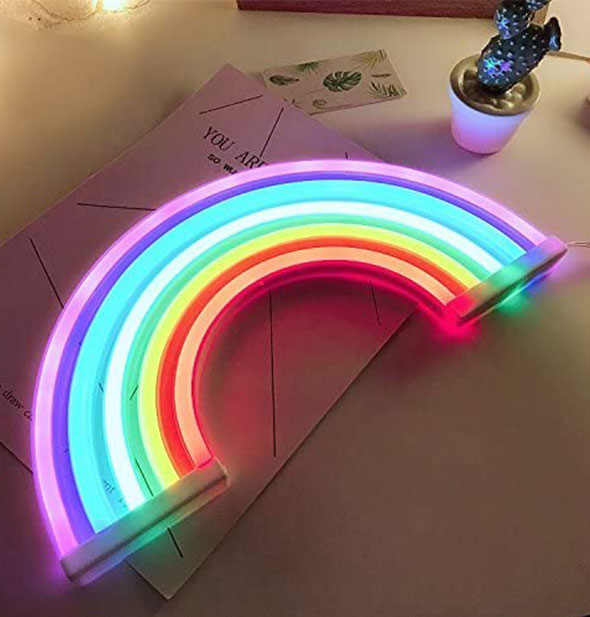 A lit rainbow neon light sits on a tabletop in a darkened room.