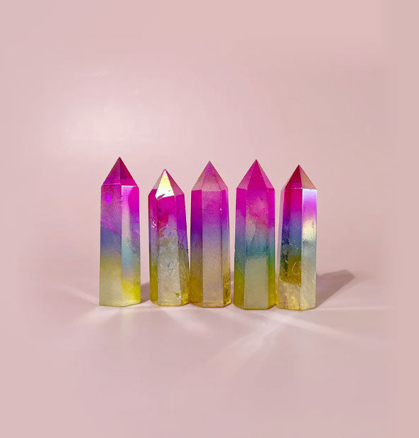 Five rainbow quartz points stood on end against a pink backdrop
