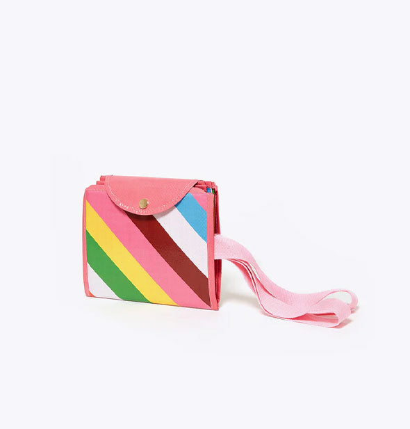 Striped tote bag shown folded into a small pouch held closed with a button snap flap and with its pink handles extending out from the side
