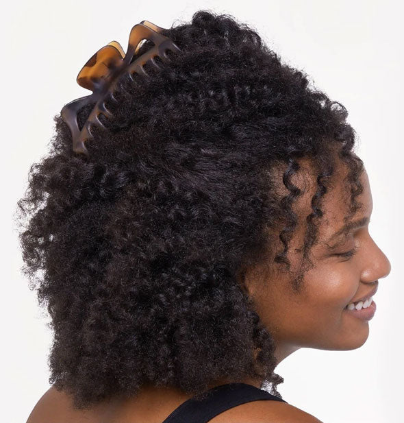 Smiling model wears a large brown tortoise claw clip in a swept-back hairstyle
